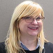 Woman with blonde hair, blue eyes, wearing glasses and a black sweater