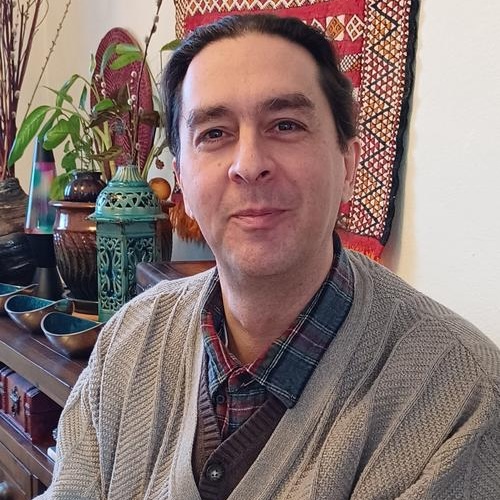 A dark haired and slightly scruffy white man looking at the camera while attempting to 