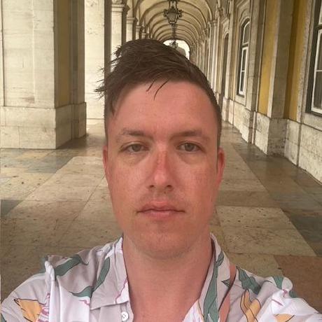 A selfie of a white man with light brown hair and a sunkissed complexion standing before a columned hall, looking somewhat aloof.