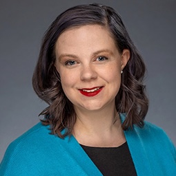 The image shows a white woman with blue curly hair and red lipstick, wearing a blue sweater over a black dress. However, my current look is dark straight hair with bangs!