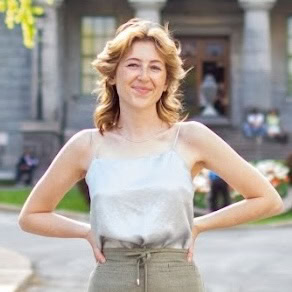 A person with light brown hair and freckles smiles and stands in front of the McGill University campus.